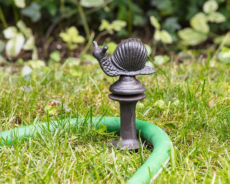 Decorative metal snail on a garden hose holder in a grassy area