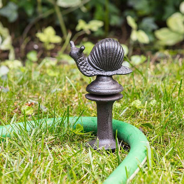 Decorative metal snail on a garden hose holder in a grassy area