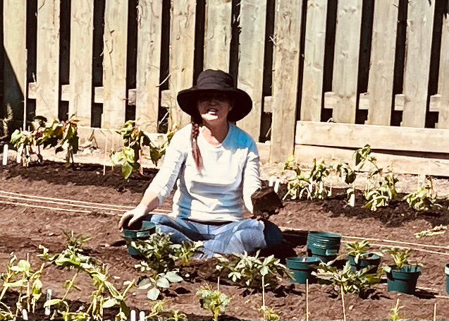Michele sitting in a garden with plants and a wooden fence in the background