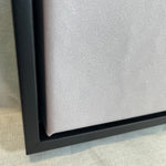 Close-up of a black framed canvas on a textured surface
