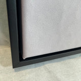 Close-up of a black framed canvas on a textured surface