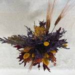 Photo from above of a dried flower arrangement in warm earthy colours against a textured white background