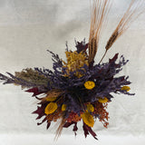 Photo from above of a dried flower arrangement in warm earthy colours against a textured white background
