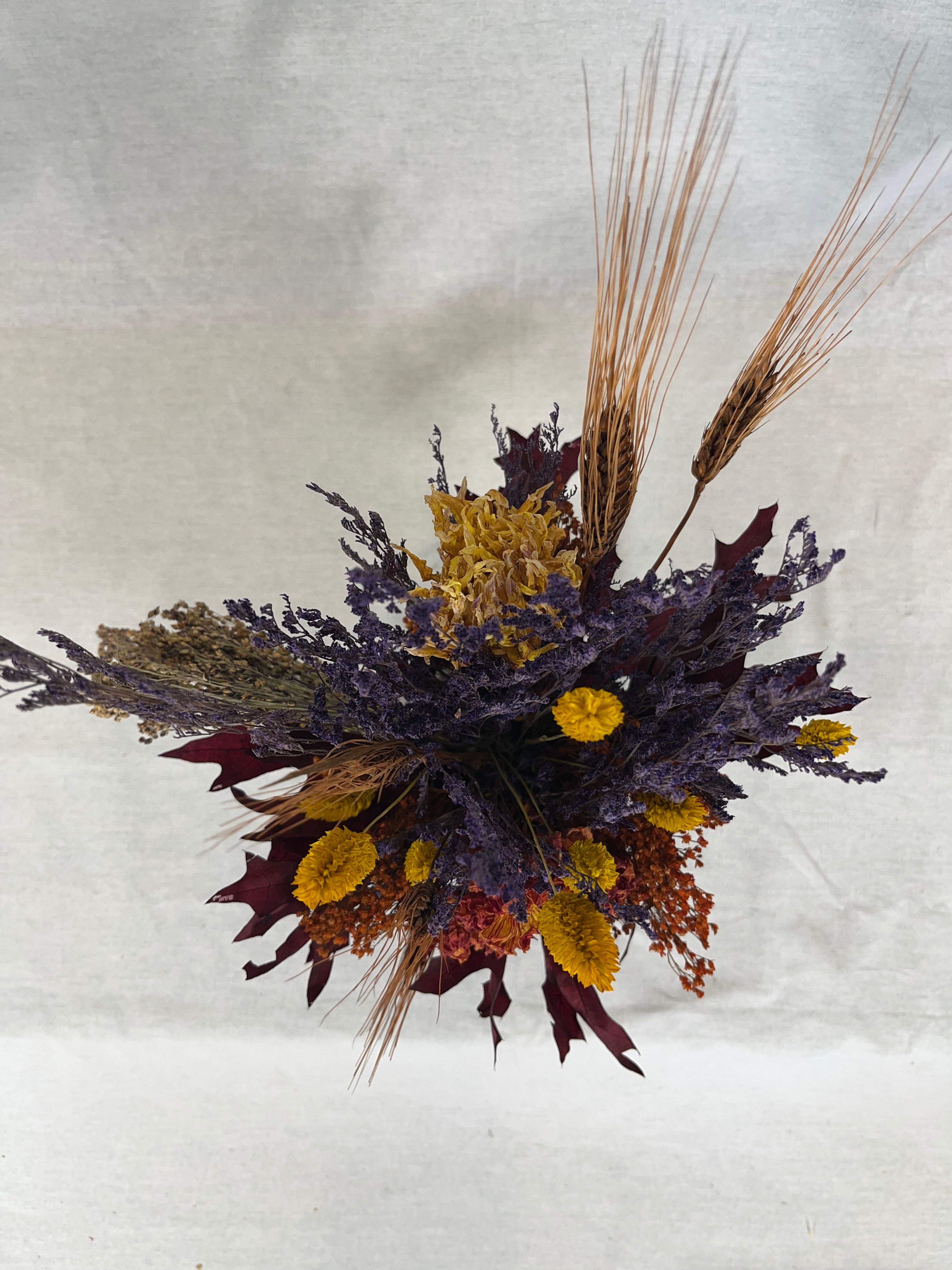 Photo from above of a dried flower arrangement in warm earthy colours against a textured white background