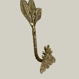 Decorative brass wall hook with leaves and a bee on a beige background