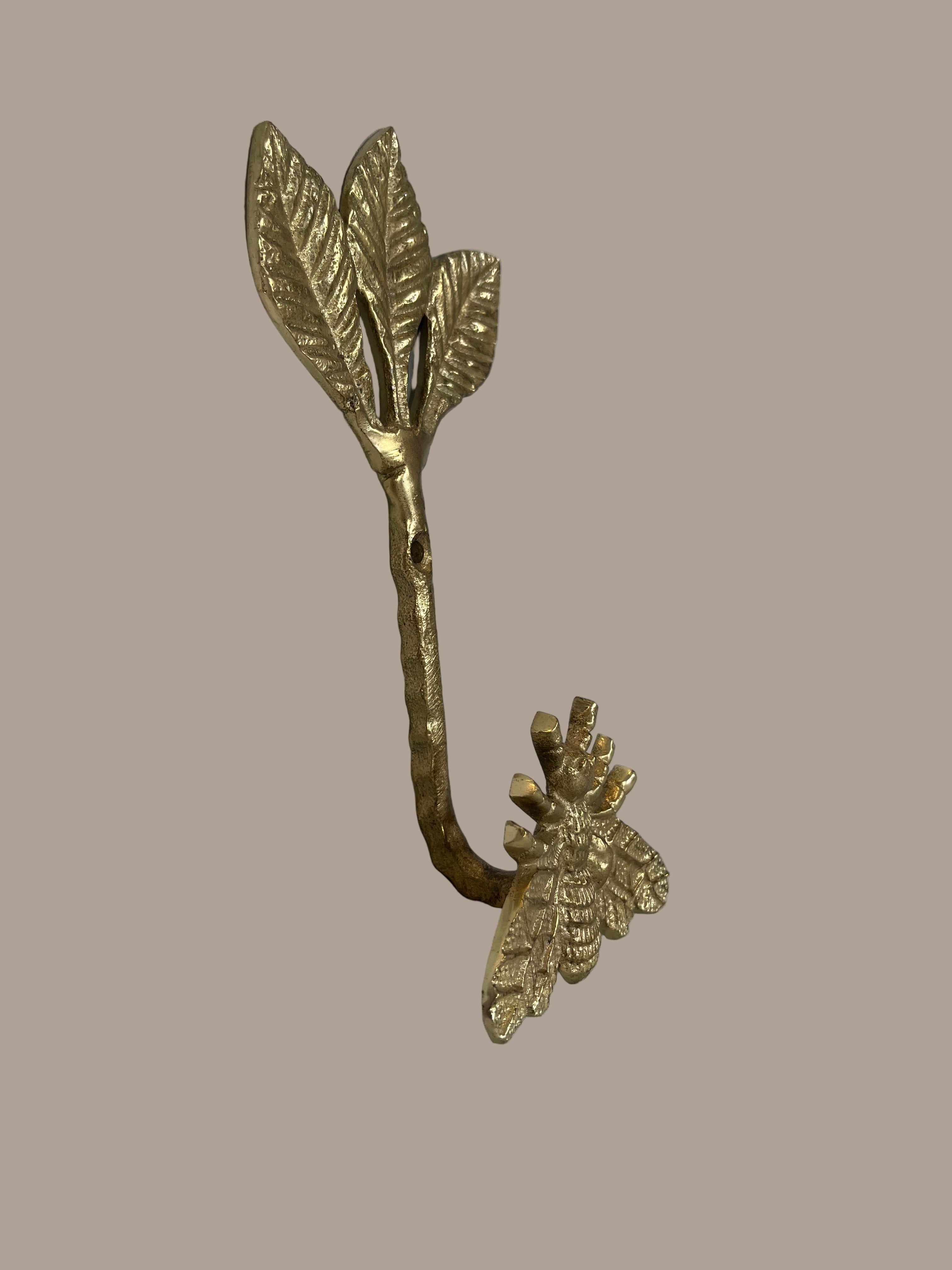 Decorative brass wall hook with leaves and a bee on a beige background