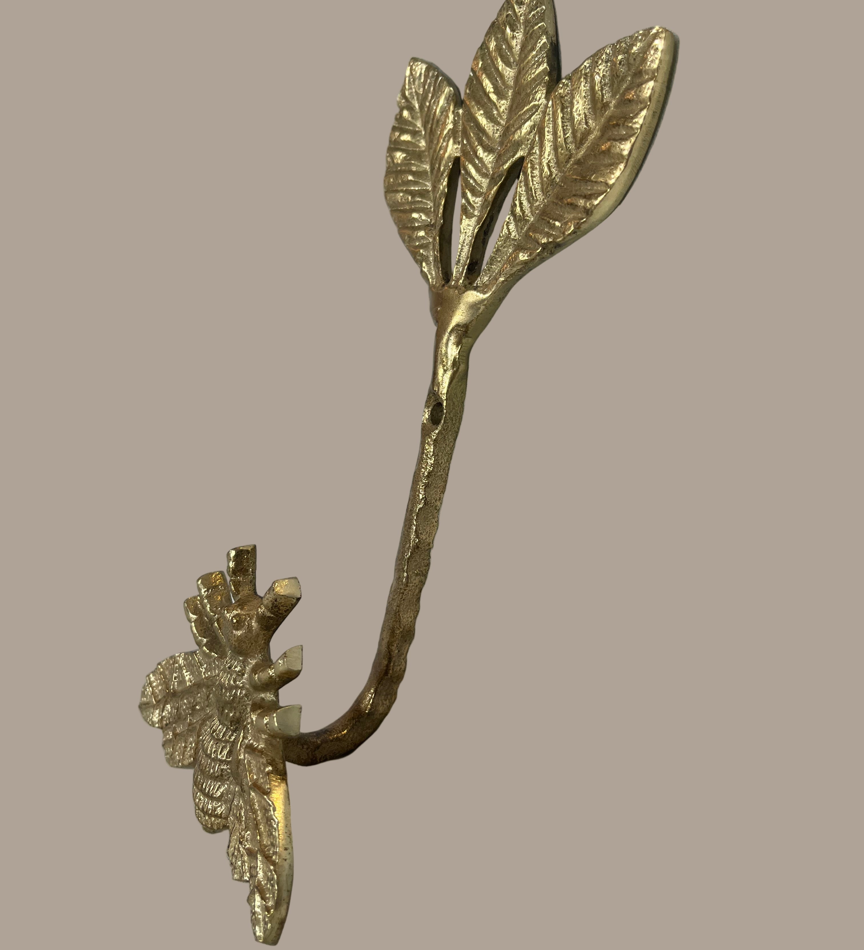 Decorative gold leaf-shaped hook with bee on a beige background