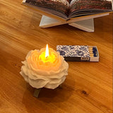 Floral-patterned candle on a wooden surface with matches and an open book in the background