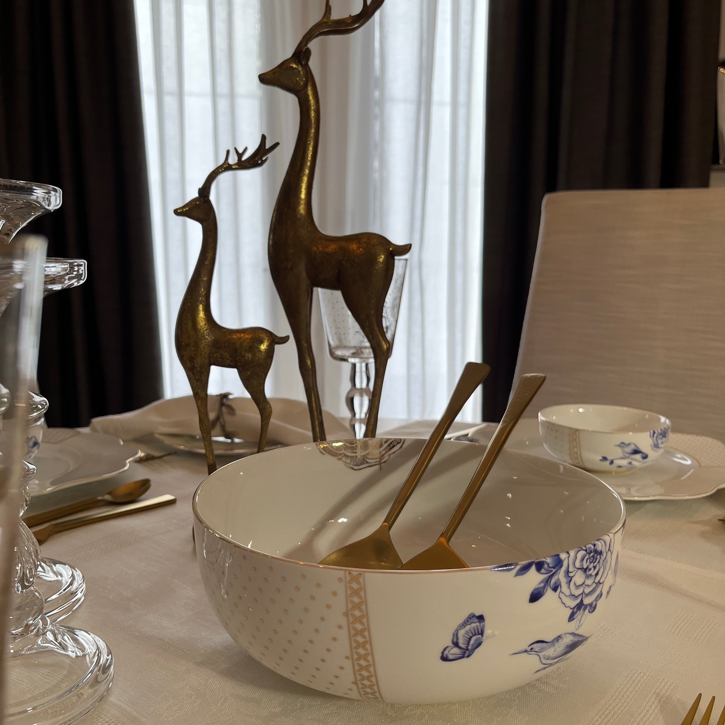 Elegant table setting featuring Pip Studio Royal White serving bowl and our Gilded Ribbon Salad Serving Set, and a pair of decorative gold reindeer as a centrepiece.
