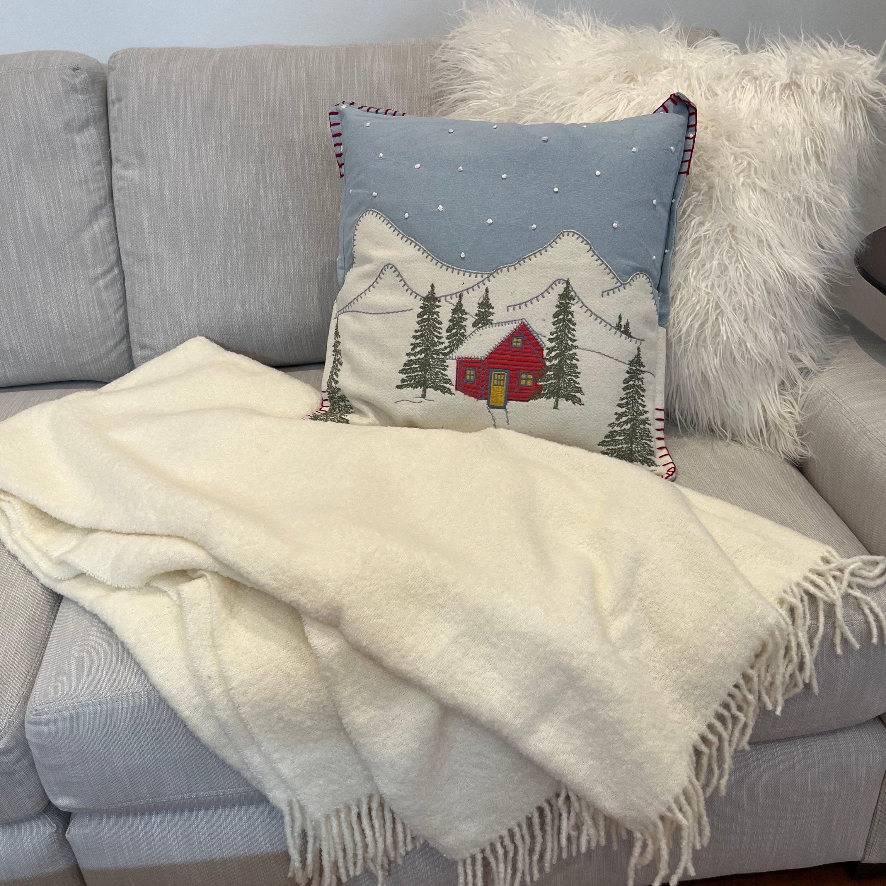 Gray sofa with a ivory wool blend throw blanket and decorative pillow featuring a red house design.