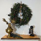 Eugene the Moose Bronze Bust in uniform sporting a monocle with his large antlers and sombre expression. He is shown here with a holiday wreath, with iron bells and an antique telephone. 