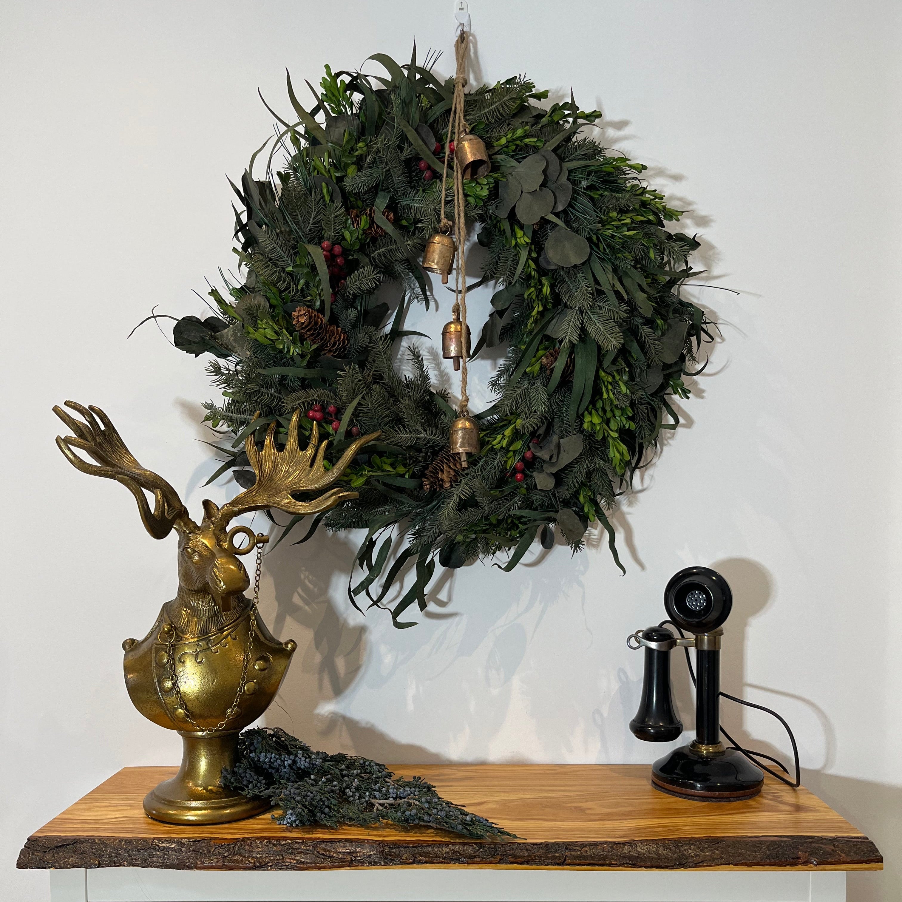 Eugene the Moose Bronze Bust in uniform sporting a monocle with his large antlers and sombre expression. He is shown here with a holiday wreath, with iron bells and an antique telephone. 