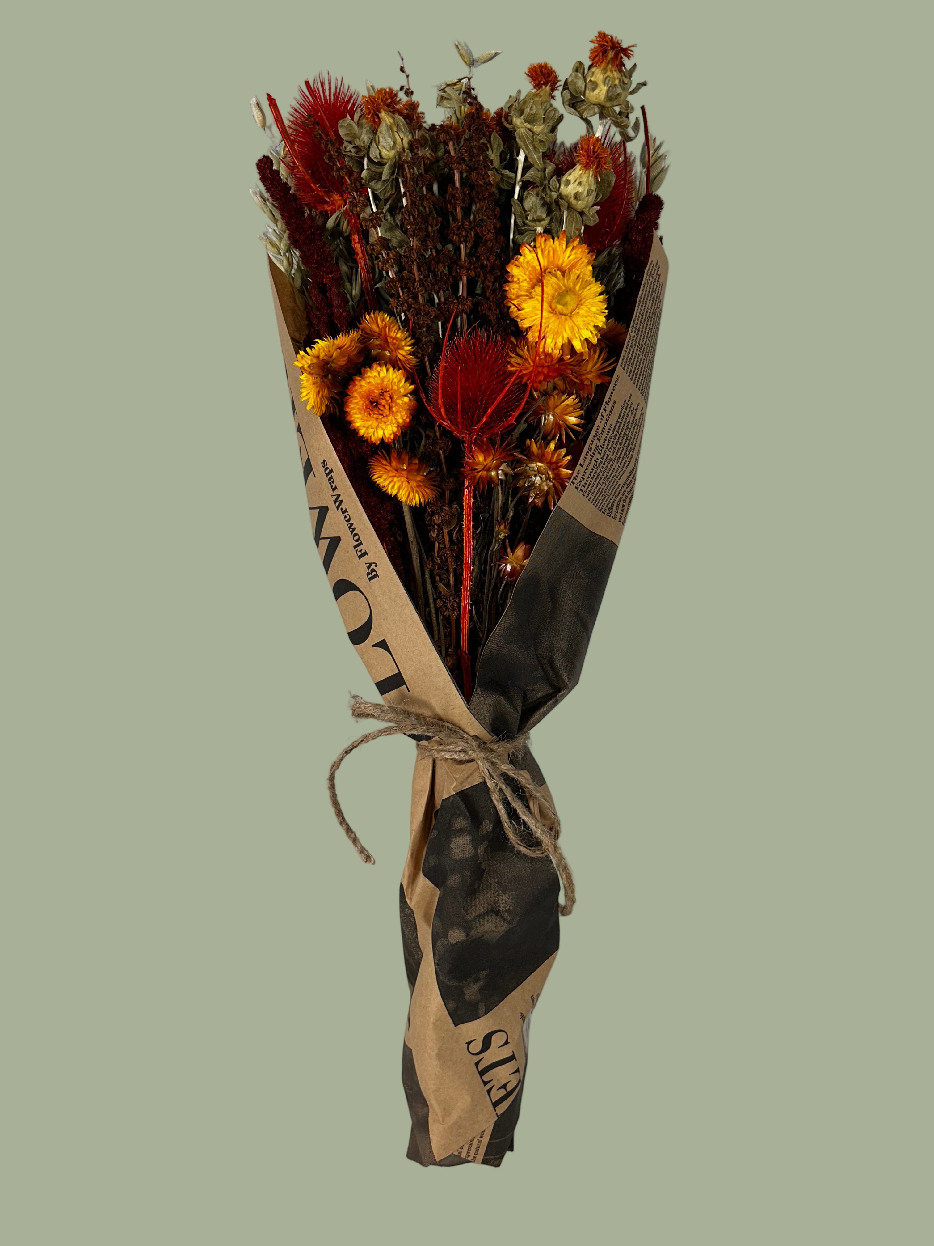 Bouquet titled "Autumn Ember Bouquet" is designed to be a magnificent focal point, perfect for a large vase on a dining table, an entryway, or a mantelpiece. In this photo it is wrapped in bouquet paper that looks like vintage newspaper against a plain green background.