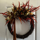 Decorative asymmetrical wreath that blends rustic textures with rich autumnal colours, accented with a rich brown velvet ribbon hung on a white door