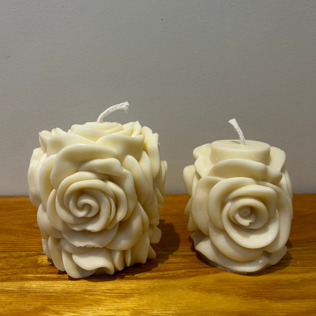 Two natural soy wax candles with a blooming rose design on a wooden surface with a plain background