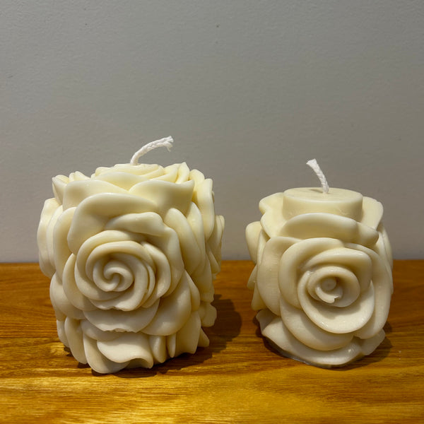 Two natural soy wax candles with a blooming rose design on a wooden surface with a plain background