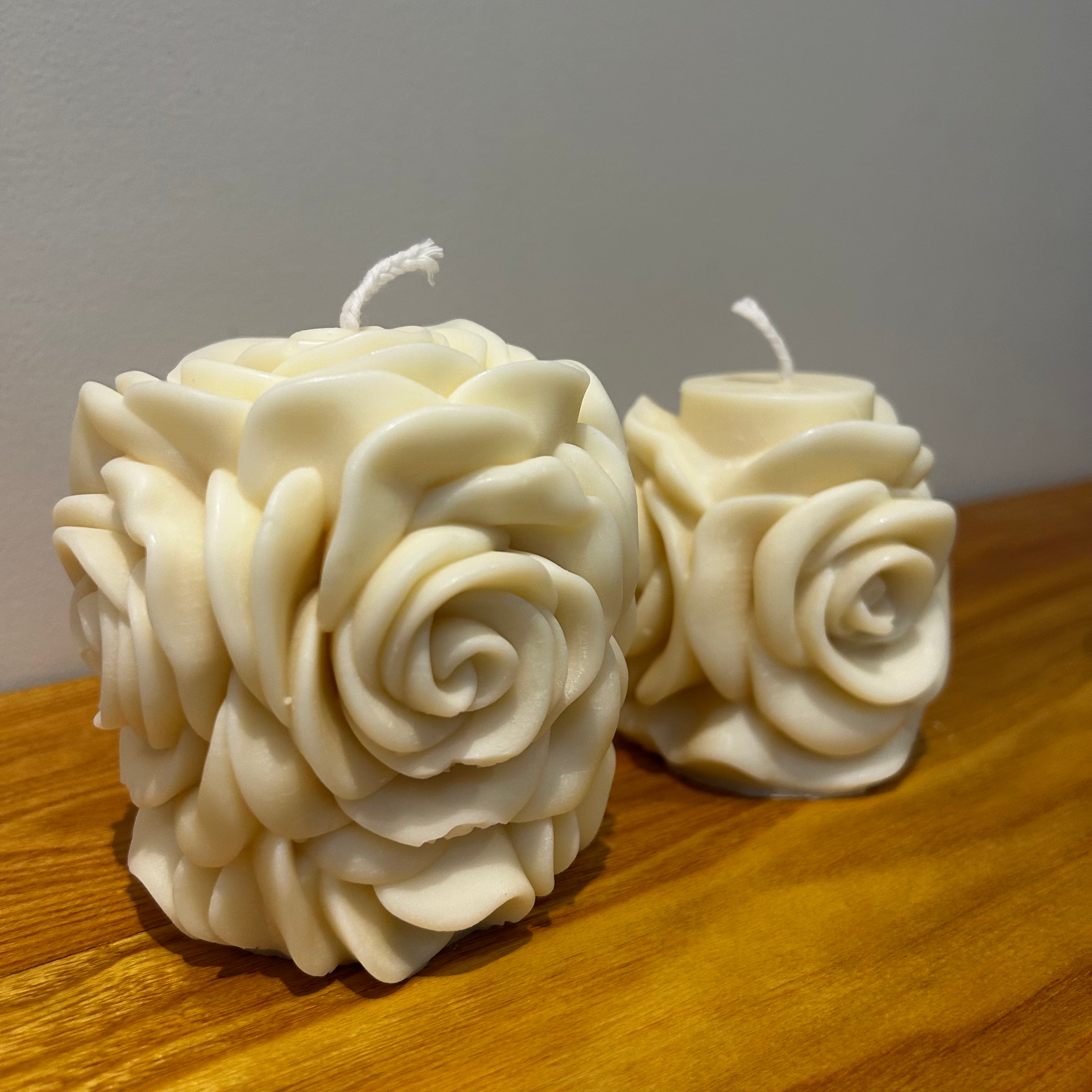 Two natural soy wax candles with a blooming rose design on a wooden surface with a plain background