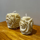 Two natural soy wax candles with a blooming rose design on a wooden surface with a plain background