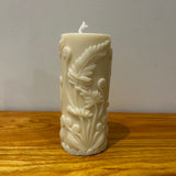 Decorative white pillar candle embossed with fern pattern on a wooden surface