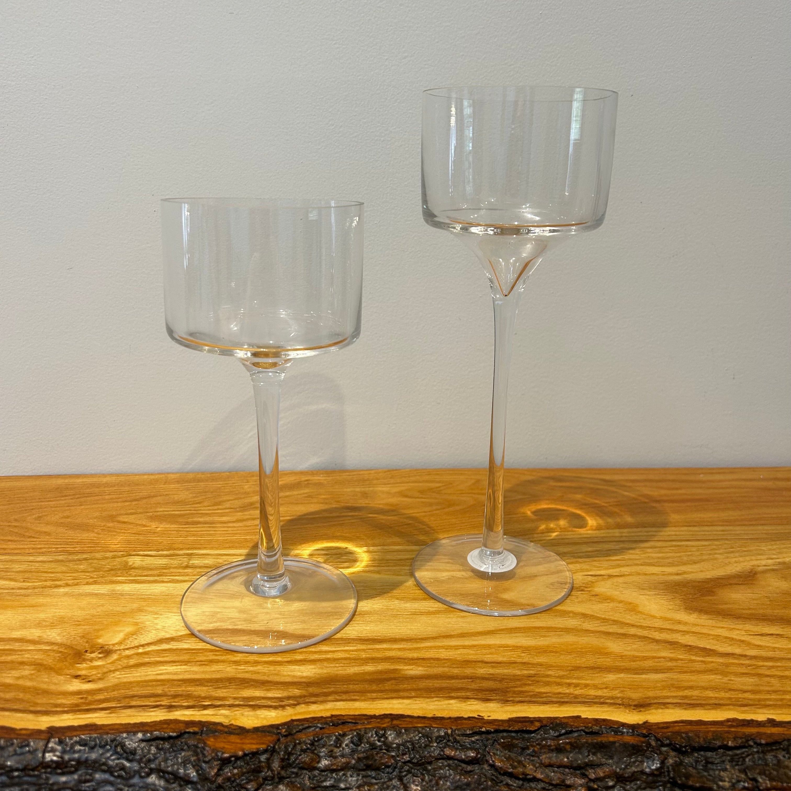 Two clear glass stemmed candle holders shaped like goblets on a wooden surface with a neutral background