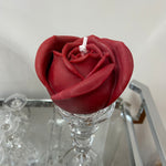 A beautiful handcrafted candle with intricate detailing of a red rose shape made from 100% pure vegan soy wax. on a glass stand with a neutral background
