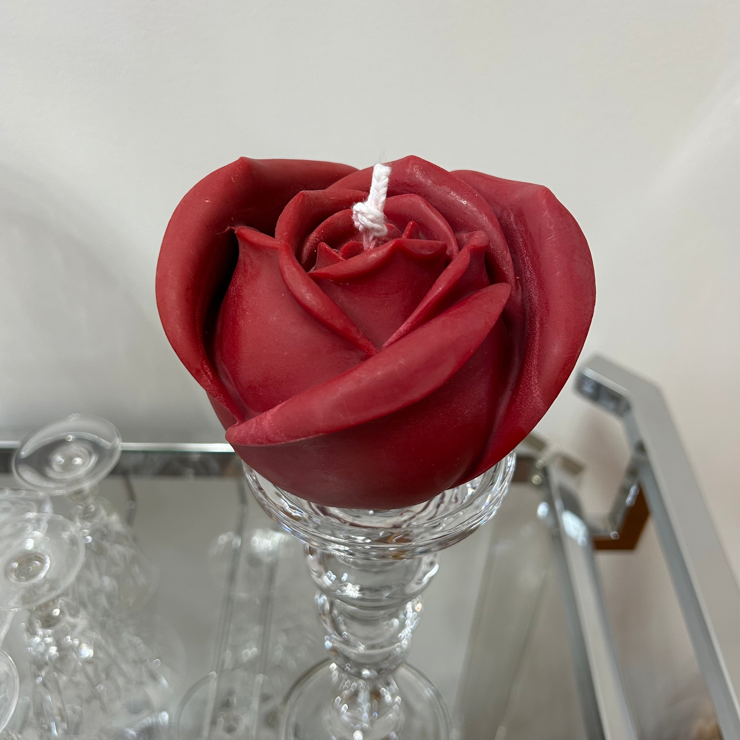 A beautiful handcrafted candle with intricate detailing of a red rose shape made from 100% pure vegan soy wax. on a glass stand with a neutral background