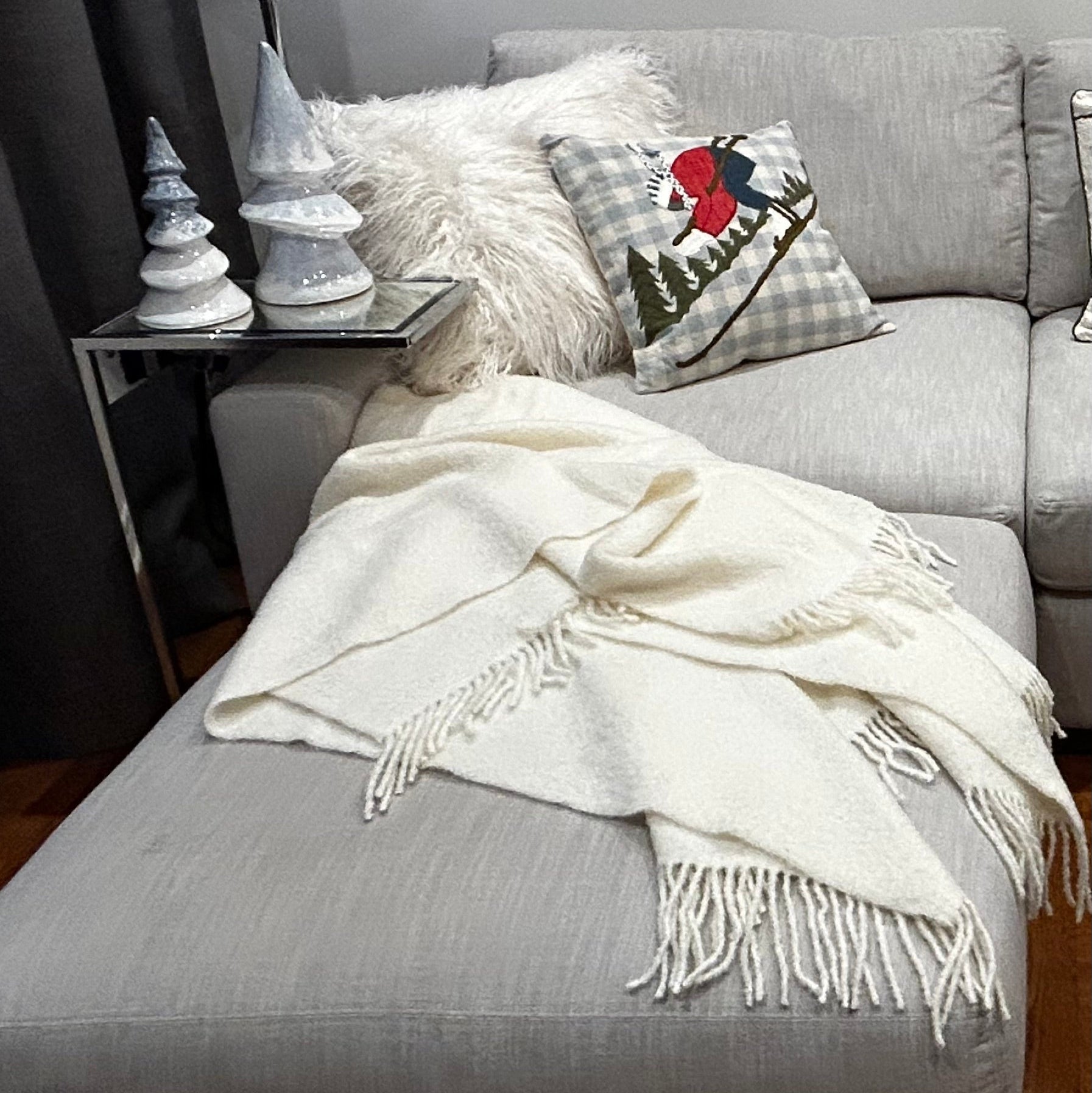 Grey sofa with a our Fireside Embrace Throw, decorative pillows, and small Christmas trees on a side table.