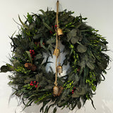 A wreath featuring a stunning foundation of deep green preserved spruce and preserved boxwood, beautifully layered with the modern forms of dried green curly eucalyptus and large round leaf eucalyptus. Traditional accents of red berries and natural pinecones are nestled throughout, completing this breathtaking tapestry of texture and colour. Accessorized with a beautiful set of hand-made iron bells with a bronze finish hanging on jute twine.