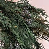 A close up of a wreath layered with lush, preserved Cedar and accented with vibrant Juniper Berries,