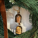 Close up of a wreath layered with lush, preserved Cedar and accented with vibrant Juniper Berries, a chocolate brown velvet bow with ribbon ends dangling, and a pair of iron bells on jute twine hanging in the middle.