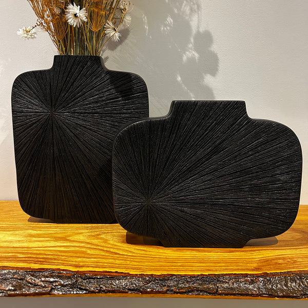 Two striking, sculptural vases in midnight-cocoa with a bold, radiating carved pattern that starting in the left corner. One vase is tall while the other is wide.