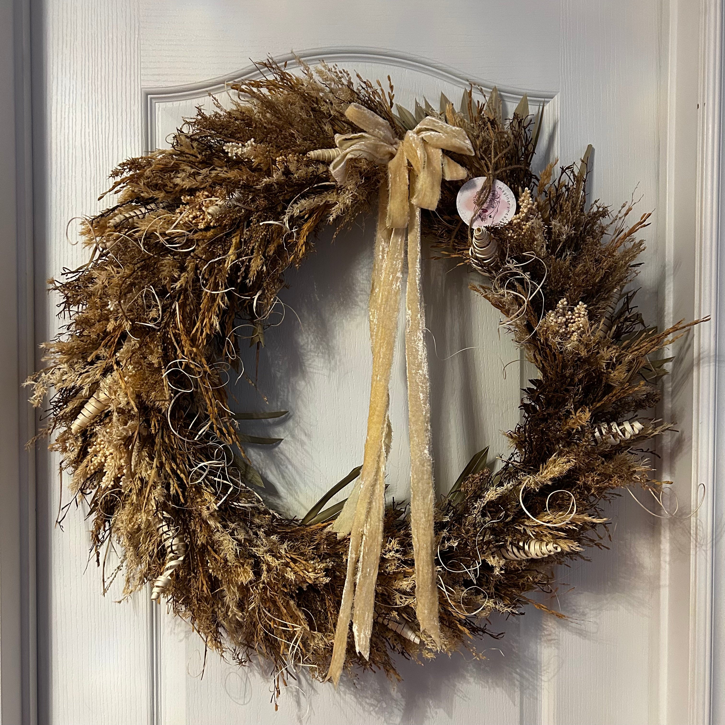 This impressive 28 inch wreath is made with the elegance of spider wood and the airy lightness of Star Grass. It is a rich tapestry of grains, including the unique forms of Sorghum, dried Rice Ears, and graceful Arena Wild Oats. Sculptural bleached cane cones and the whimsical twists of bleached curly ting ting add the final, enchanting touches.
