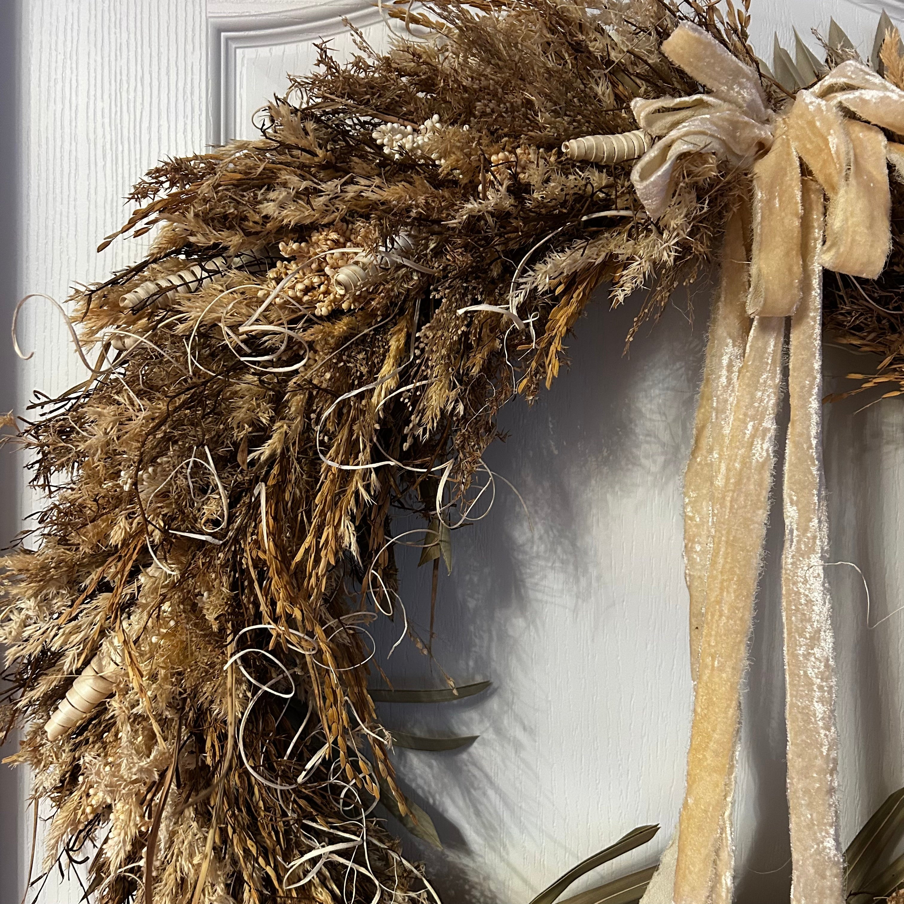 A close-up of this impressive 28 inch wreath is made with the elegance of spider wood and the airy lightness of Star Grass. It is a rich tapestry of grains, including the unique forms of Sorghum, dried Rice Ears, and graceful Arena Wild Oats. Sculptural bleached cane cones and the whimsical twists of bleached curly ting ting add the final, enchanting touches.