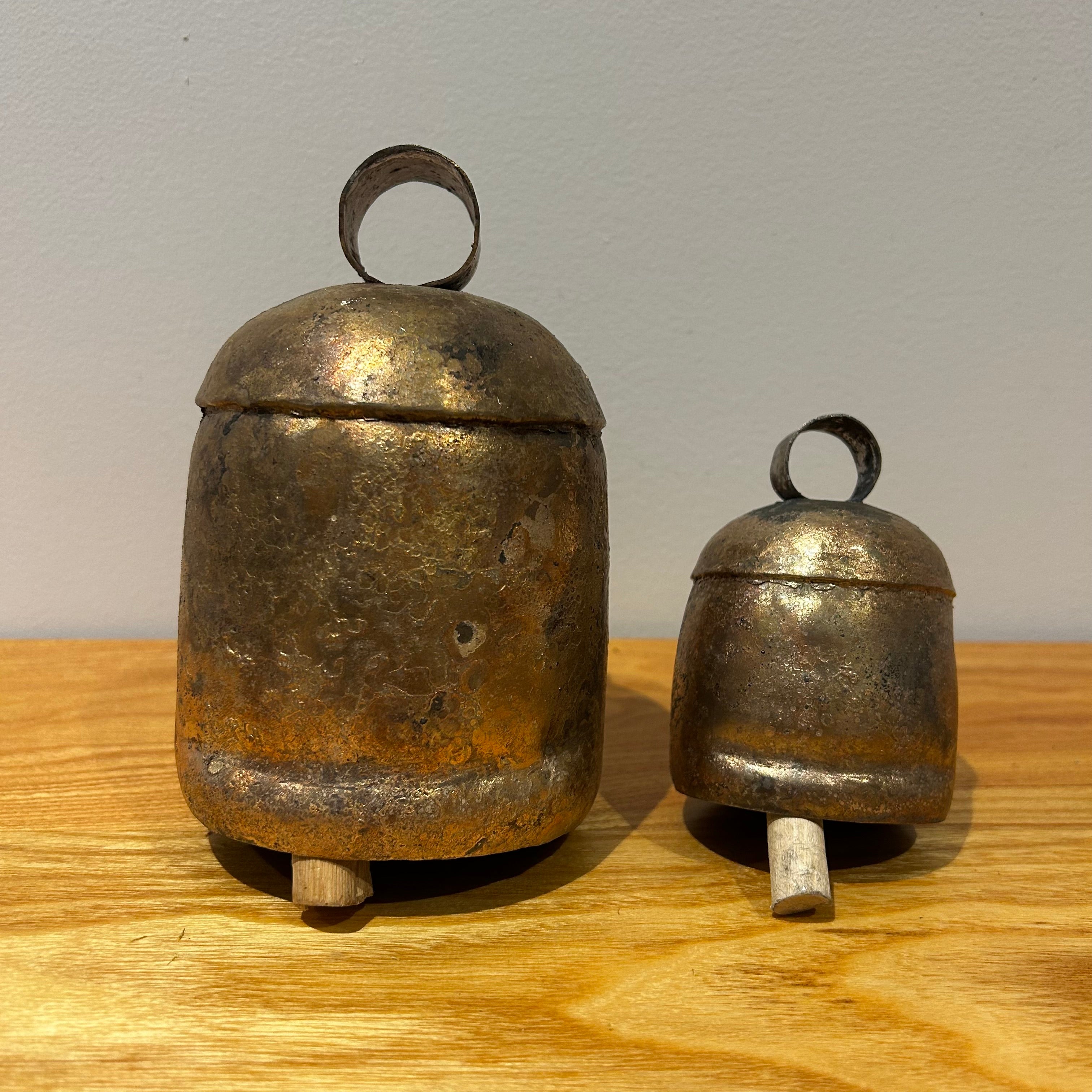 Two vintage inspired bronze coloured bells on a wooden surface against a light background