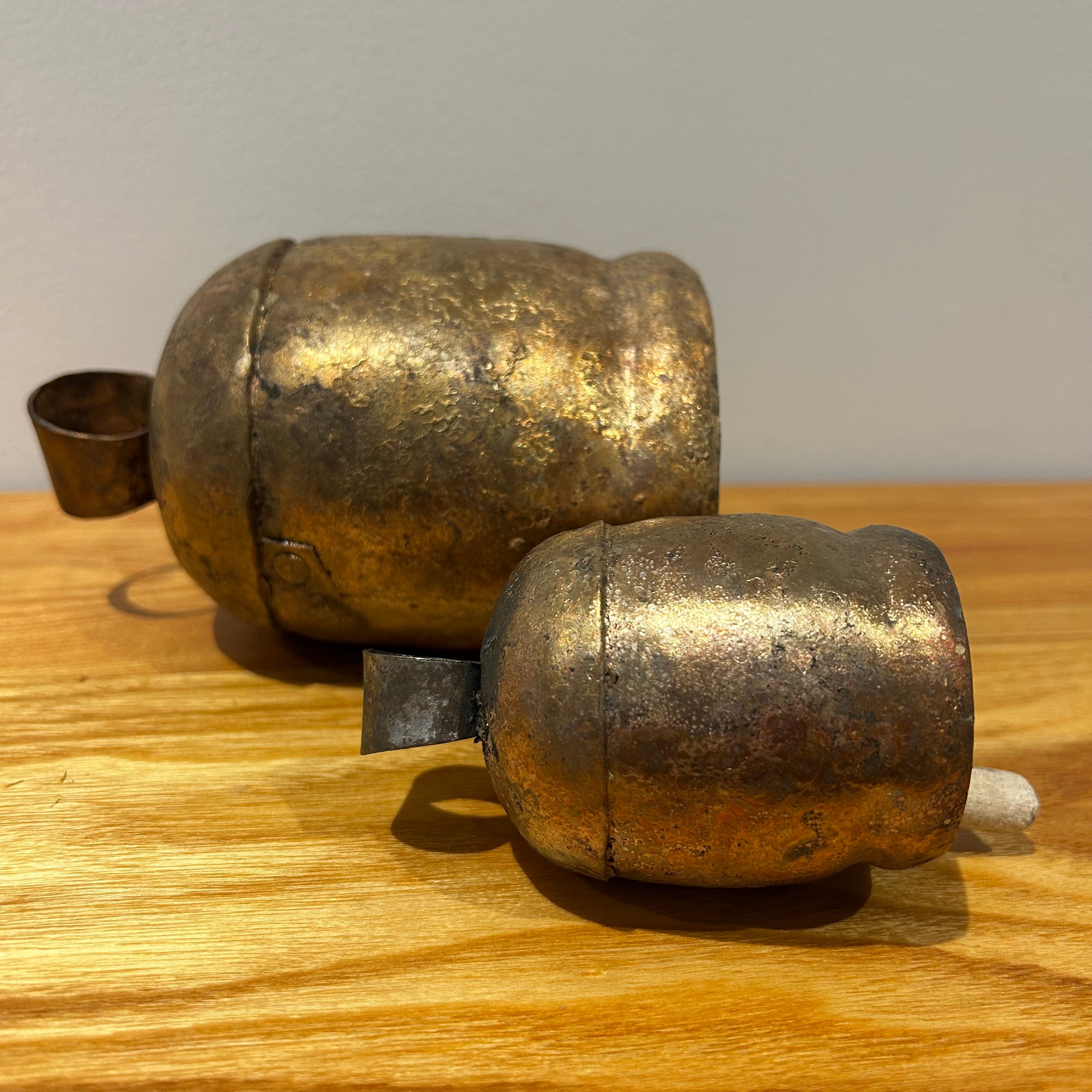 Two vintage inspired bronze coloured bells laying on their side on a wooden surface against a light background