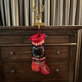Decorative bronze deer head stocking holder hook on a wooden dresser holding a beautiful  decorative hand-knit stocking with a hand-embroidered wreath. The deer is quite a character wearing glasses and smoking a pipe. 