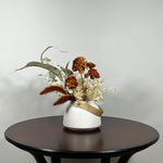 Dried flower arrangement with slender stems of natural green willow eucalyptus reach out from one side, complemented on the opposite side by the soft, bleached plumes of Calamgrostis canadensis. Ethereal Lunaria in pristine white adds a delicate, luminous quality. The featured floral is a cluster of five Dahlia stems, their petals a beautiful rust tone that gracefully fades into a vibrant golden heart, a perfect echo of the setting sun.