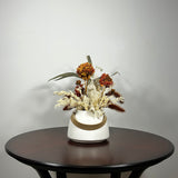 Dried flower arrangement with slender stems of natural green willow eucalyptus reach out from one side, complemented on the opposite side by the soft, bleached plumes of Calamgrostis canadensis. Ethereal Lunaria in pristine white adds a delicate, luminous quality. The featured floral is a cluster of five Dahlia stems, their petals a beautiful rust tone that gracefully fades into a vibrant golden heart, a perfect echo of the setting sun.