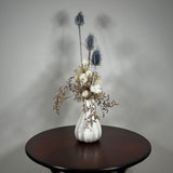 Vase of dried floral arrangement made with delicate, lace-like petals of white Cape Flowers against the intriguing, sculpted heads of blue Teasels. Adding airy lightness and enduring colour is German Statice. 