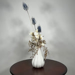 Vase of dried floral arrangement made with delicate, lace-like petals of white Cape Flowers against the intriguing, sculpted heads of blue Teasels. Adding airy lightness and enduring colour is German Statice. 