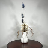 Vase of dried floral arrangement made with delicate, lace-like petals of white Cape Flowers against the intriguing, sculpted heads of blue Teasels. Adding airy lightness and enduring colour is German Statice. 