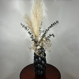 This dried floral arrangement has soft, elegant plumes of natural Pampas Grass reach gracefully upward, complemented by the bold, preserved forms of blue Eucalyptus and the airy lightness of German Statice (sea lavender). The delicate whimsy of bleached Triticum (wheat) wisps adds a touch of rustic charm, while soft white Cape Flowers provide subtle pops of pure, natural colour.