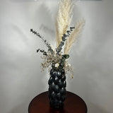 This dried floral arrangement has soft, elegant plumes of natural Pampas Grass reach gracefully upward, complemented by the bold, preserved forms of blue Eucalyptus and the airy lightness of German Statice (sea lavender). The delicate whimsy of bleached Triticum (wheat) wisps adds a touch of rustic charm, while soft white Cape Flowers provide subtle pops of pure, natural colour.