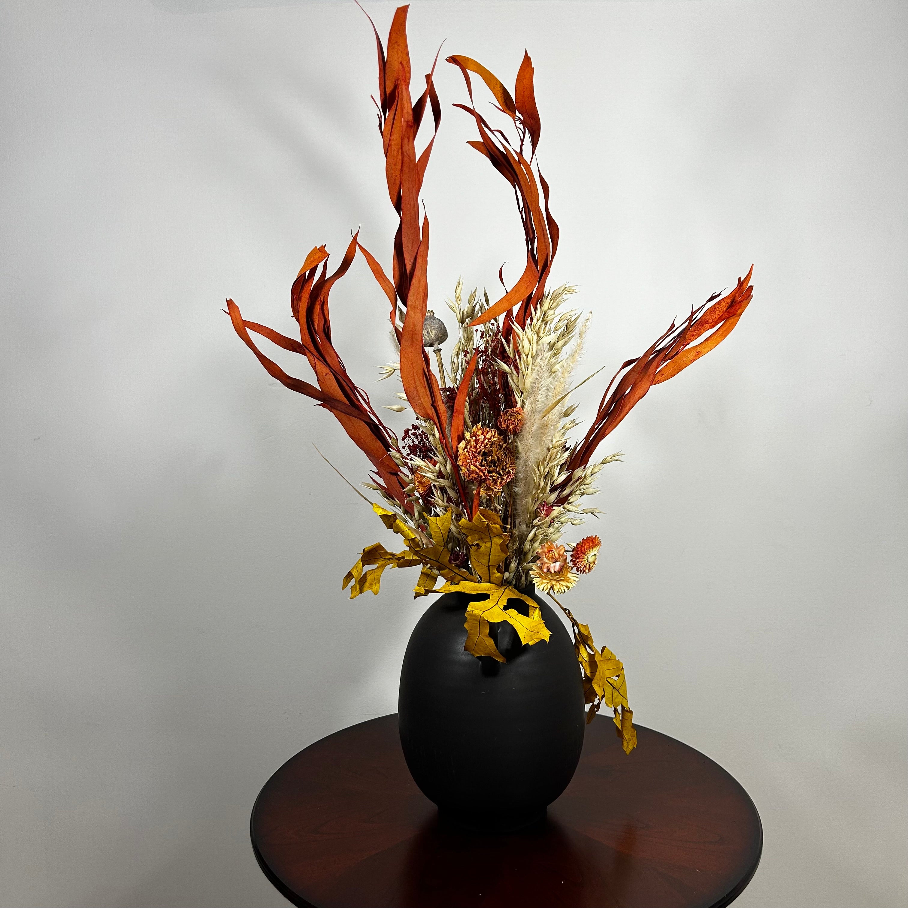 A magnificent 30" dried floral arrangement with autumn botanicals like helichrysum, dahlias, & oak leaves in a matte brown urn.