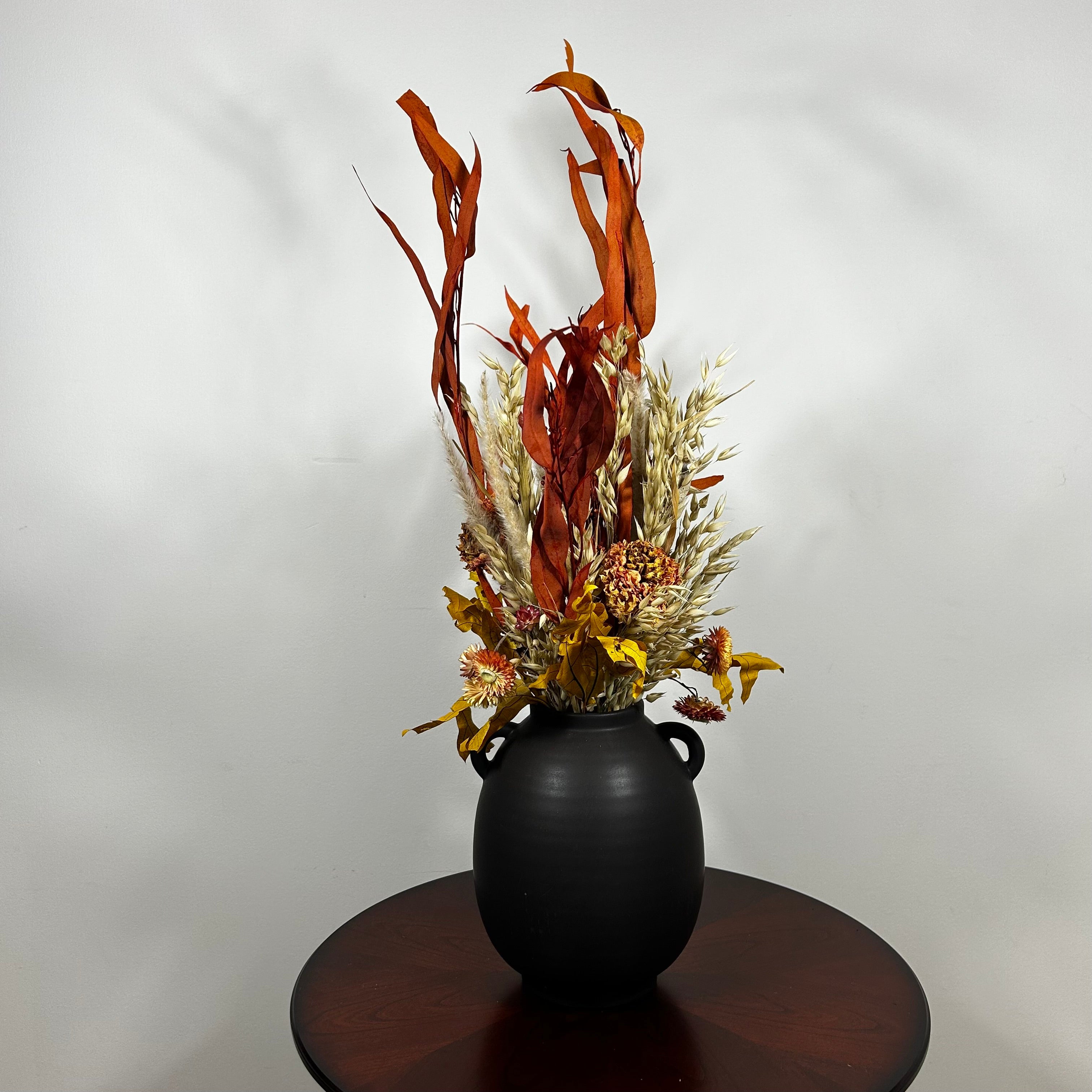 A magnificent 30" dried floral arrangement with autumn botanicals like helichrysum, dahlias, & oak leaves in a matte brown urn.