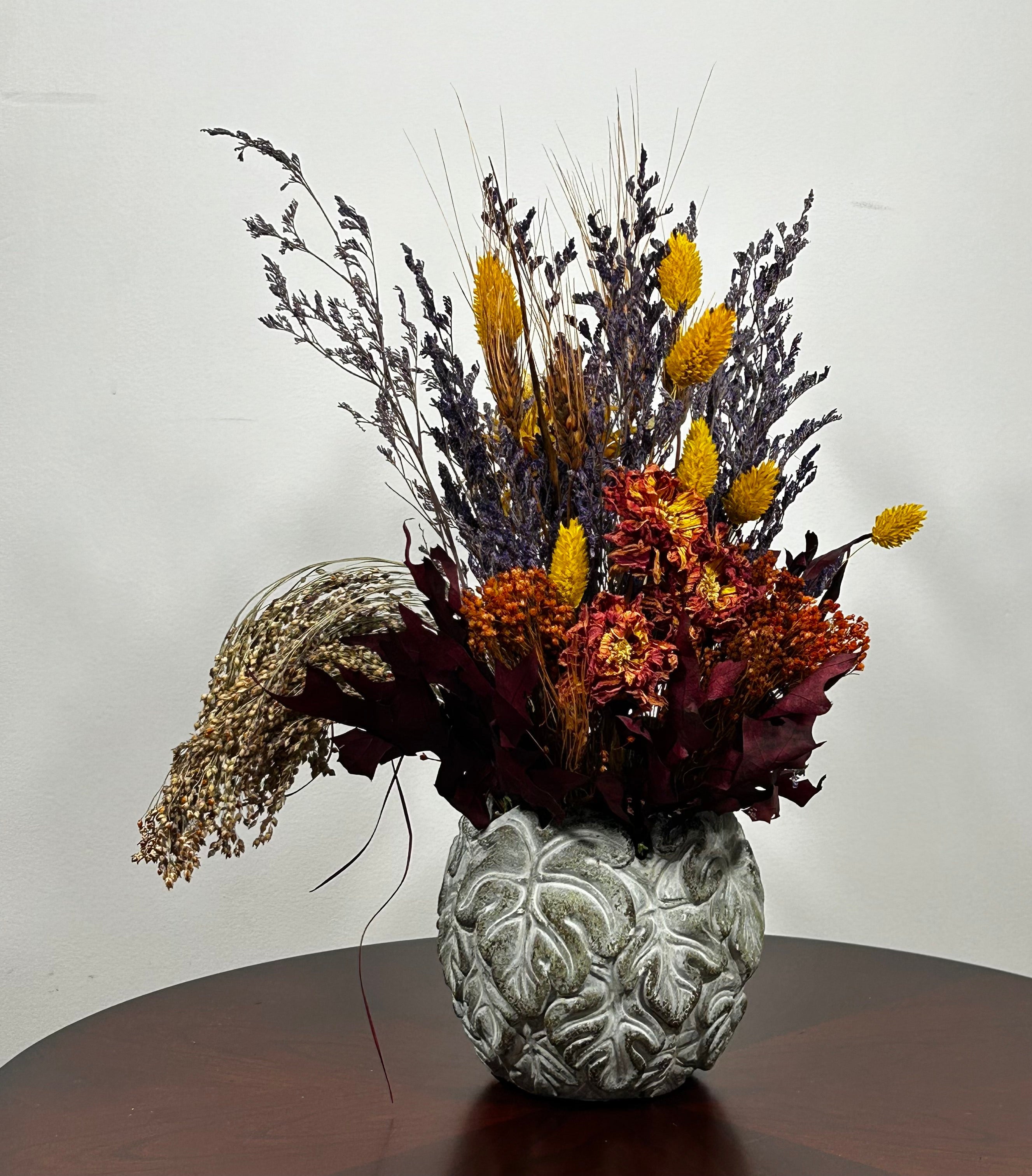 Decorative vase with dried flowers on a wooden surface against a white wall