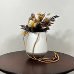 White hanging planter with beautiful dried flowers arrangement with burgundy bracken, ivory helichrysums, Nigel seed pods, natural teasels, and ivory phalaris on a beige background