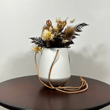 White hanging planter with beautiful dried flowers arrangement with burgundy bracken, ivory helichrysums, Nigel seed pods, natural teasels, and ivory phalaris on a beige background