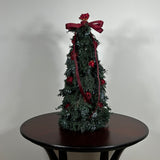Decorative Christmas tree this 18-inch design is densely layered with fragrant, preserved Juniper and its signature blue berries, with beautiful deep red "Bright Torch" roses are placed to command attention. The entire piece is finished with a large, elegant deep red grosgrain double bow, whose ribbons cascade down.