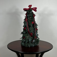 Decorative Christmas tree this 18-inch design is densely layered with fragrant, preserved Juniper and its signature blue berries, with beautiful deep red "Bright Torch" roses are placed to command attention. The entire piece is finished with a large, elegant deep red grosgrain double bow, whose ribbons cascade down.